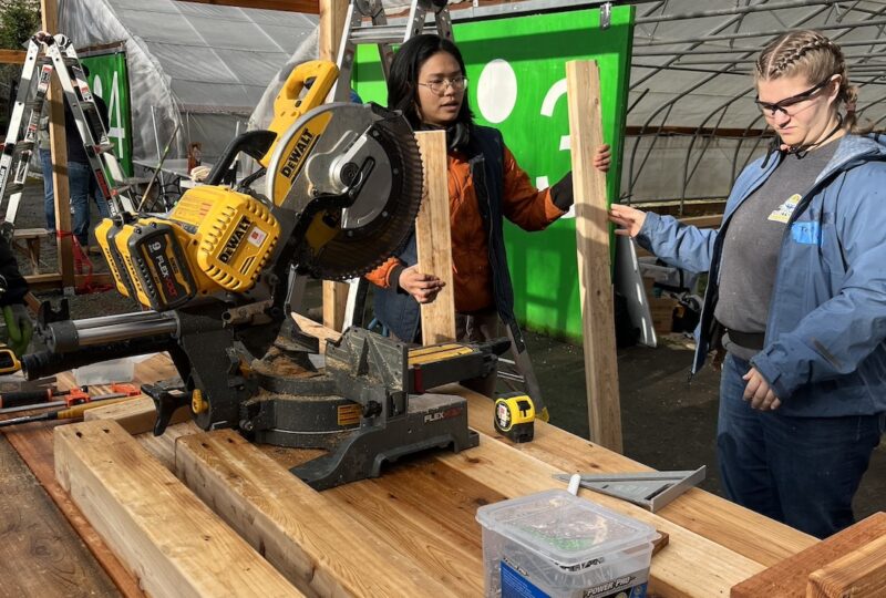 student and mentor using a saw in front of a greenhouse